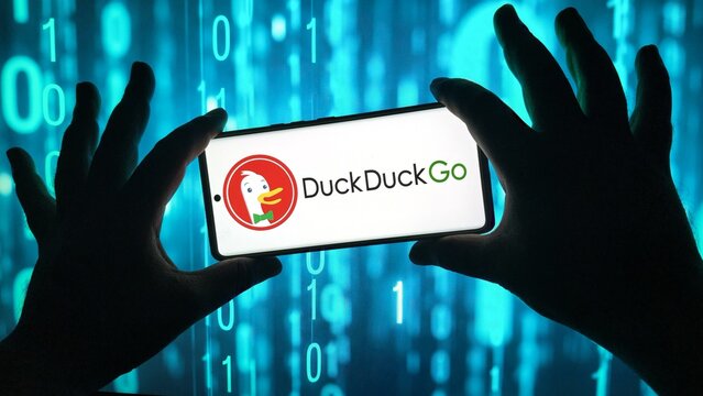 Hands holding smartphone with duckduckgo logo against binary code