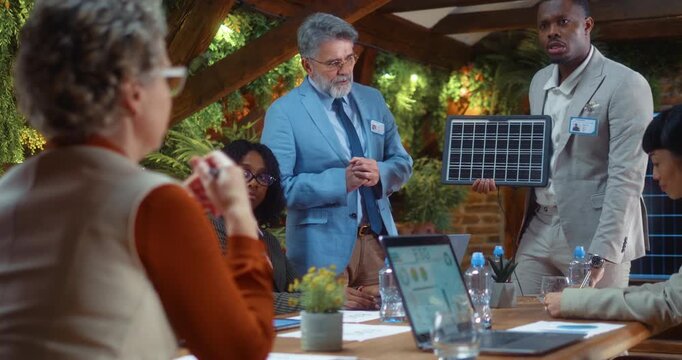 African business professional presents solar panel model during sustainability meeting, explaining innovations and engaging team discussion and collaboration in modern eco office.