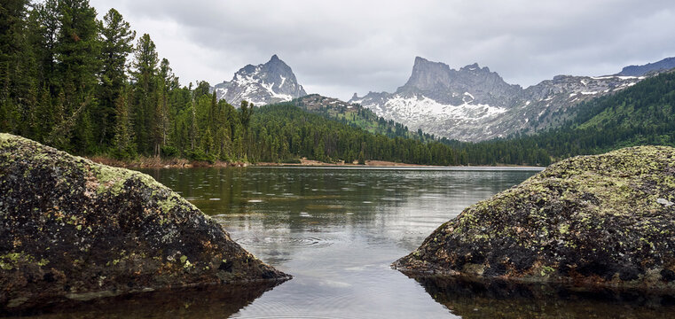 Scenic mountain lake with snow-capped peaks reflecting in still water. Serene nature landscape for travel and adventure concept. Ergaki natural park