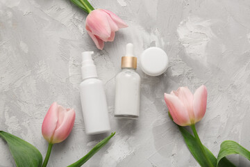 Different cosmetics and beautiful flowers on grey background