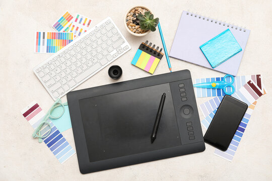 Graphic tablet with mobile phone, computer keyboard and stationery on light background, top view
