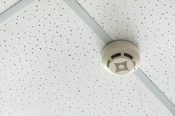 Modern smoke detector on ceiling in room, closeup