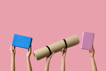 Female hands with yoga blocks and yoga mat on pink background
