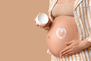 Young pregnant woman with heart made of cream on her belly against color background, closeup