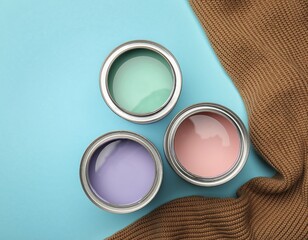 Three paint cans with pastel colors alongside a cozy knitted sweater