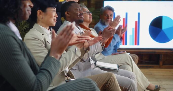 Multiracial business team applauding after a seminar or meeting, seated in a row, expressing satisfaction, approval, and positive feedback in a modern corporate training environment.