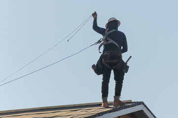 Construction worker handling fall prevention gear on the roof of a two-story wooden home under construction, representing residential roofing work and safety compliance operations