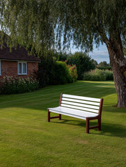 Serene garden scene with a white bench under a tree on a sunny afternoon by a cozy brick house