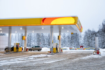 Exterior of a gas station in winter. Gasoline pumps and cars refueling on a snowy day.