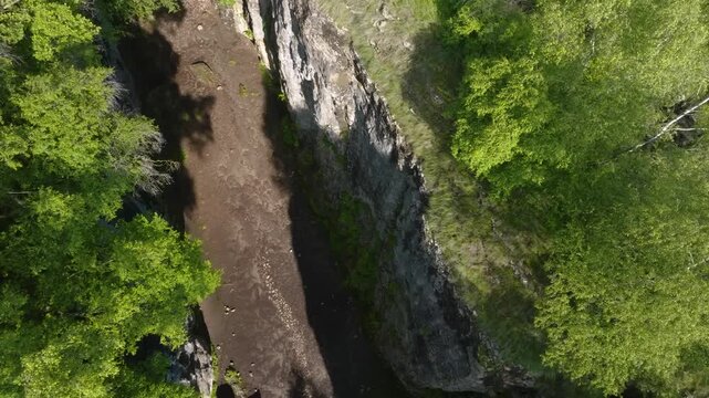 An aerial, top-down view of the narrow and deep Matlas Canyon in the Republic of Dagestan, Russia. The dramatic gorge features steep rocky walls and a dry riverbed or path below, surrounded by lush gr