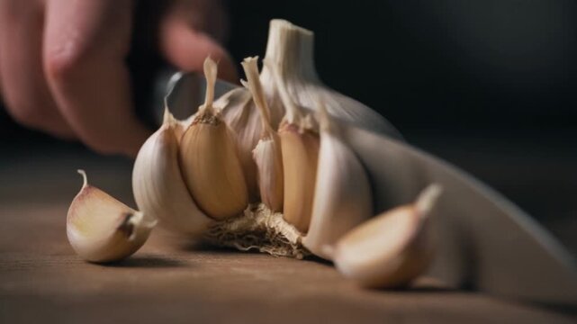 A hand uses a knife to separate fresh garlic cloves on a wooden cutting board
