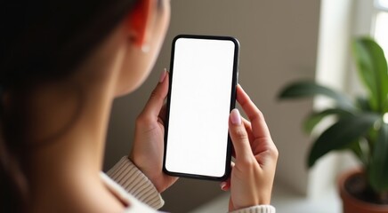 Woman holding up a phone with a white screen in front of a plant mockup