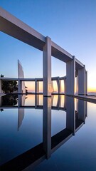 Modern white geometric building with reflecting pool at dusk
