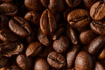 Fototapeta premium Roasted coffee beans texture background. Full frame closeup of aromatic arabica grains. Top view pattern of brown caffeine ingredient. Fresh energy drink wallpaper
