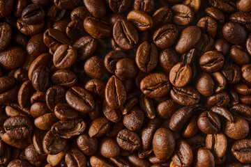 Fototapeta premium Roasted coffee beans texture background. Full frame closeup of aromatic arabica grains. Top view pattern of brown caffeine ingredient. Fresh energy drink wallpaper