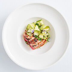 Delight in a beautifully presented grilled salmon dish, garnished with fresh cucumber and herbs