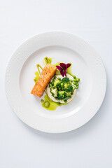 Seared salmon sits beside creamy broccoli puree, beautifully garnished with green herbs and flowers