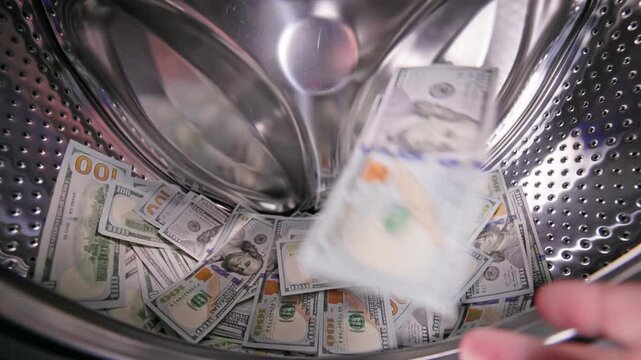 hand is adding the US Dollar banknotes inside a washing machine drum, money laundering and fraud concept.