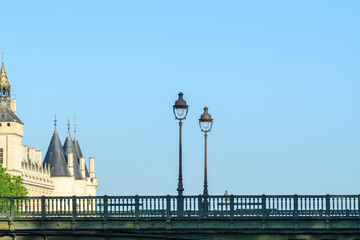 Fototapeta premium Two ornate street lamps stand on the Pont d'Arcole bridge, with historic turrets and stone architecture of central Paris visible under a clear blue sky.