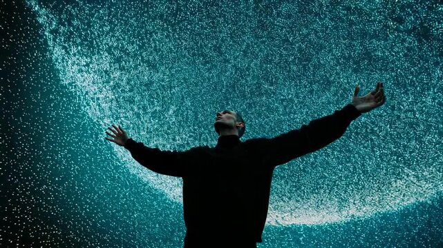 Silhouette of man standing with raised arms beneath swirling abstract blue particles expressing wonder freedom spirituality inner strength and emotional connection with cosmic energy