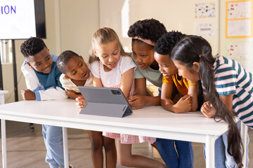 Diverse group of six school-age children gathering around tablet in gray folio case at class table