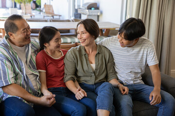 Diverse family sitting on gray couch in living room, smiling and interacting with cushions