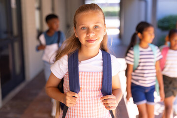 Diverse teenage students walking toward camera in shaded school corridor holding backpack straps