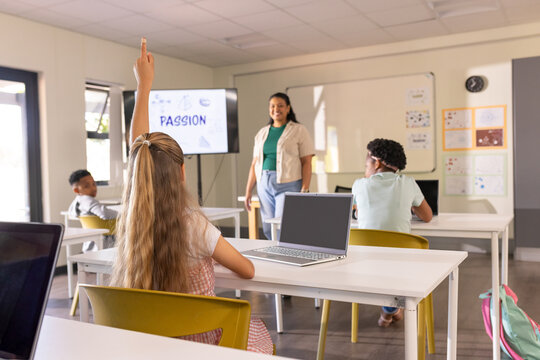 Diverse classroom teacher presenting PASSION slide while youth students raising hands with laptops