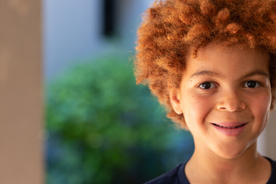 School-age African American boy smiling on porch in dark crew-neck shirt near green foliage