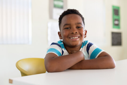 African American child sitting at white table in classroom wearing blue striped shirt smiling