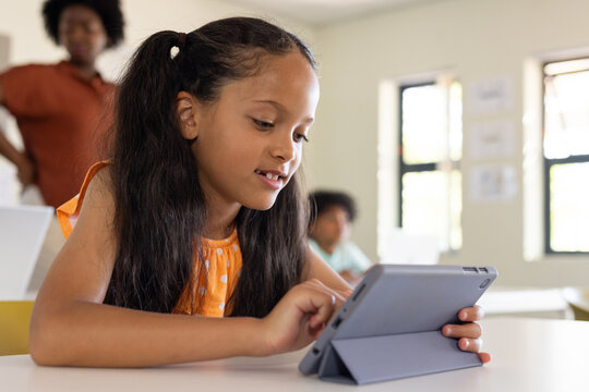 African American youth female in orange polka-dot top tapping tablet in folio at classroom desk
