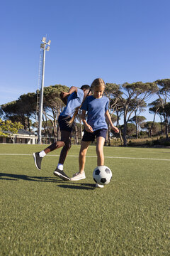 Diverse youth teammates wearing blue T-shirts dribbling on turf at sports complex with soccer ball
