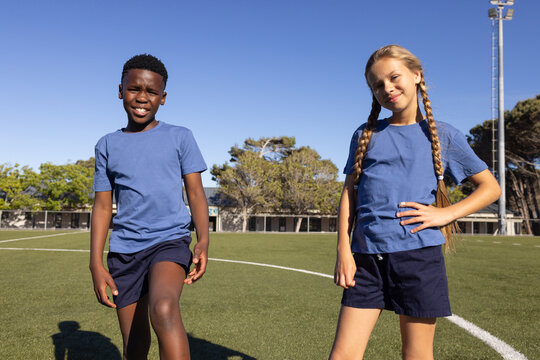 Diverse school kids wearing matching blue tees and navy shorts smiling on turf with white lines
