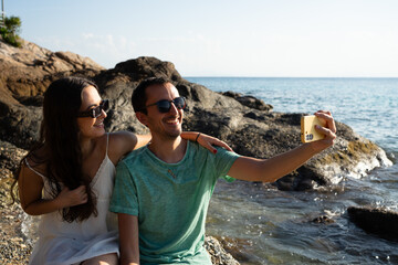 Happy couple taking selfie on rocky beach vacation