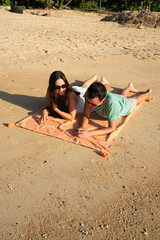 Couple smiling and lounging on a towel on the sand