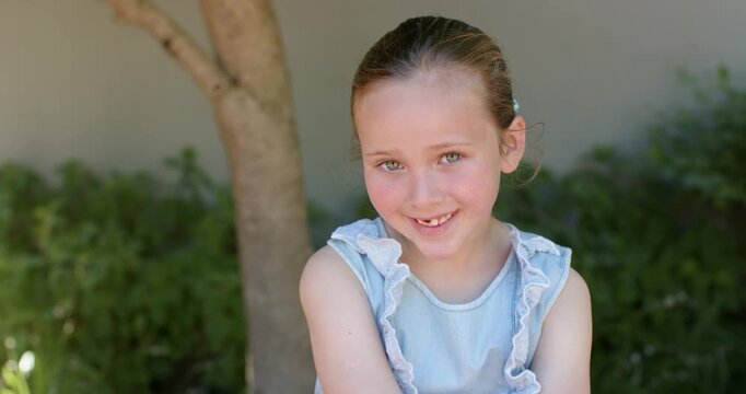 Female child 7-9 smiling and tilting head to off-camera cue in backyard, wearing ruffled blue top