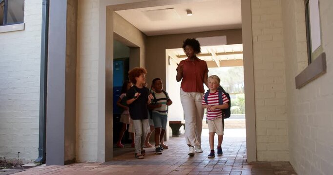 African American teacher with kids greeting boy handing tablet, leading out to yard with backpacks