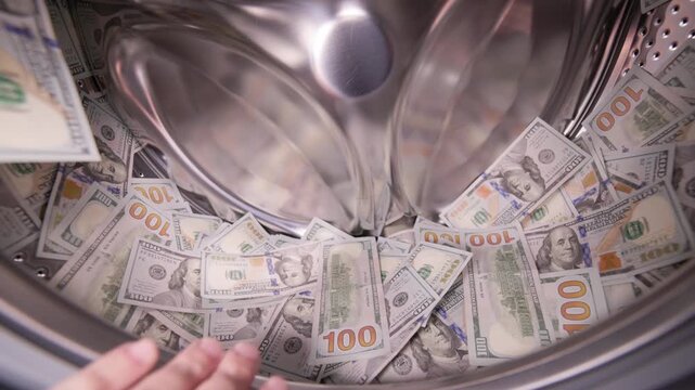 Hand putting USA Dollar banknotes in a washing machine drum. Money laundering concept.