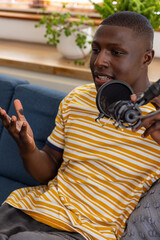 African american man speaking into podcast microphone on boom arm in home studio on sofa