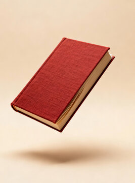 A thick cloth-bound book in muted red, mid-fall, shot from slightly below angle.