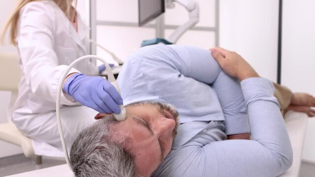 Sonographer examines brain of adult man by placing ultrasound transducer on temple of patient's head