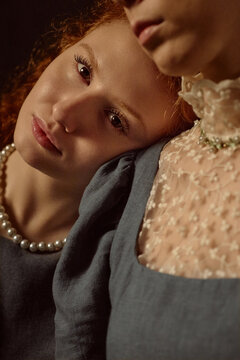 Portrait of Caucasian young adult woman resting head on shoulder of another Caucasian young adult woman, both wearing vintage style clothing, showing close emotional connection