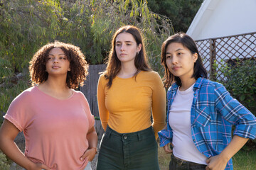 Obraz premium Diverse female friends standing in backyard amid garden shrubs, lattice trellis and wooden fence