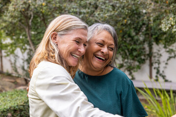 Fototapeta premium Diverse female friends hugging each other in residential garden with lush greenery backdrop