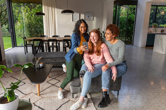 Diverse female friends sitting on bench in living area with smartphone showing prosthetic leg