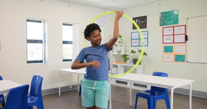 African-American teenage girl lifting neon hula hoop, swinging, practicing in class wearing shorts