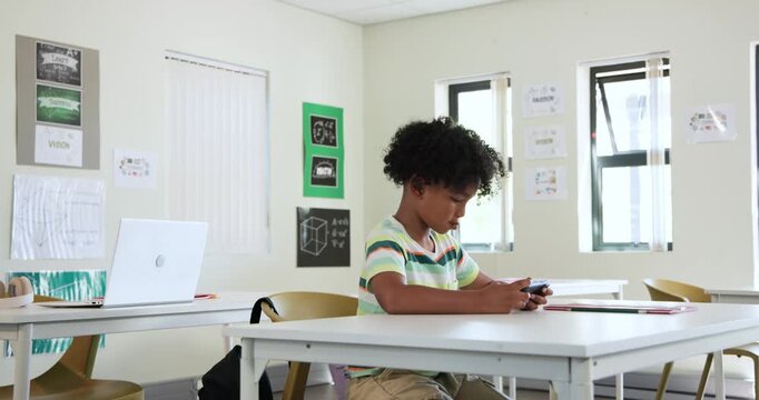 African child male holding handheld device initiating tapping and scrolling at classroom desk