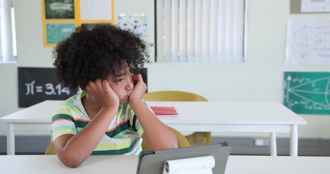 African child male school-age starting viewing tablet on stand at desk, pencil present turning left