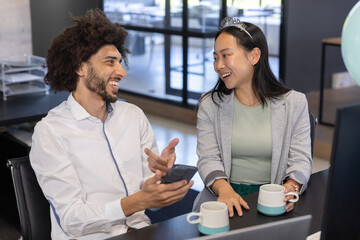 Diverse coworkers in business attire celebrating birthday at office desk with phone, headband
