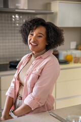 Mid adult african american woman leaning on quartz counter in home kitchen, orange juice carafe